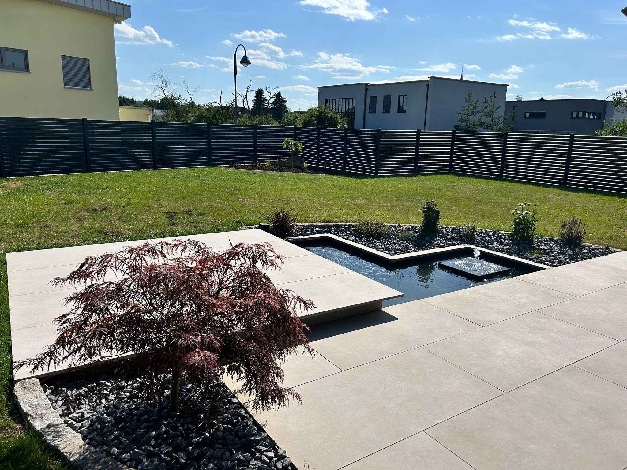 Helle Terrasse mit Wasserspiel, Pflanzbeeten und Grünfläche in Siershahn/Wirges